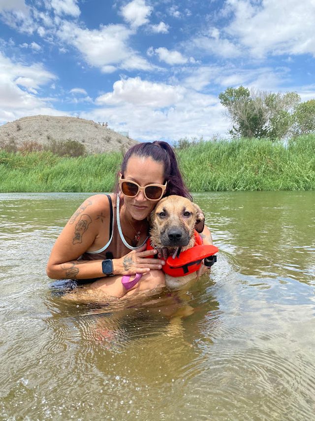 Shiann Bowman in a river, smiling, holding a rescue dog wearing a life vest