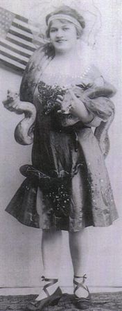 Agnes E. Sukowaty Morris, billed as Princess Naldu, posing in her snake-charmer costume in front of an American flag, holding a live snake, circa 1920s.